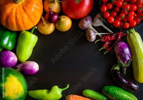 Autumn still life with pumpkin, watermelon, and a variety of colorful vegetables on black wooden background. Happy Thanksgiving background with copy space. Fresh organic food, close up.