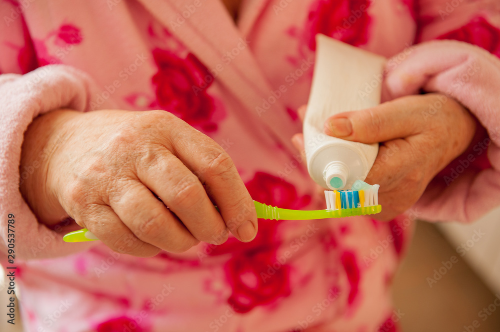 Elderly grandmother in pink terry bathrobe brushes her teeth in bathroom. Hygienic procedures. Pensioners in sanatorium Elderly grandmother in pink terry bathrobe brushes her teeth in bathroom. Hygienic procedures. Pensioners in sanatorium
