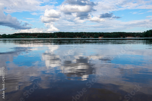 Clouds are reflected in the lake near the forest.
