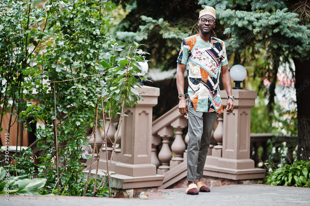 Obraz premium Handsome afro american man wearing traditional clothes, cap and eyeglasses in modern city.