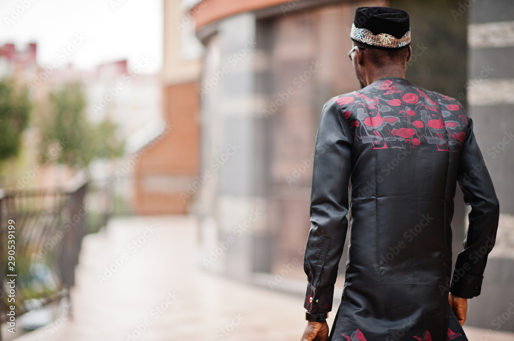 Naklejka premium Back of handsome afro american man wearing traditional clothes, cap and eyeglasses in modern city.