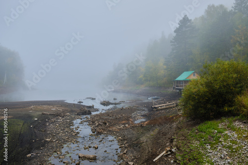House hunting on the shore of the lake at dawn in the fog. Log home, lake mist