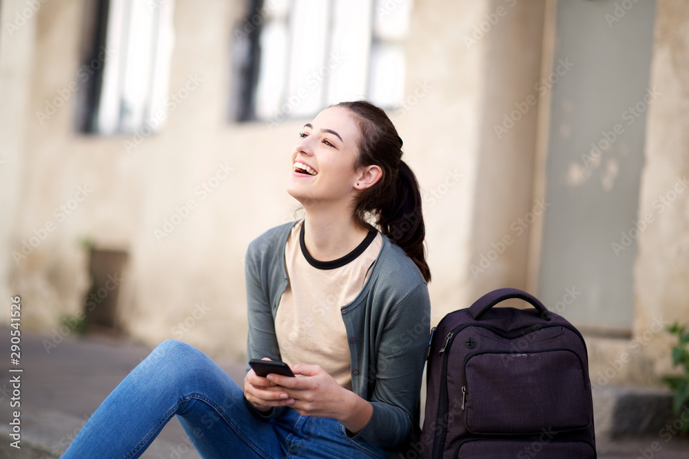 happy female student sitting outside with bag and mobile phone happy female student sitting outside with bag and mobile phone