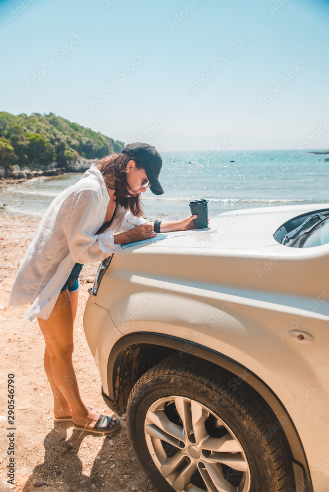 woman checking map on car hood drinking coffee at summer sea beach