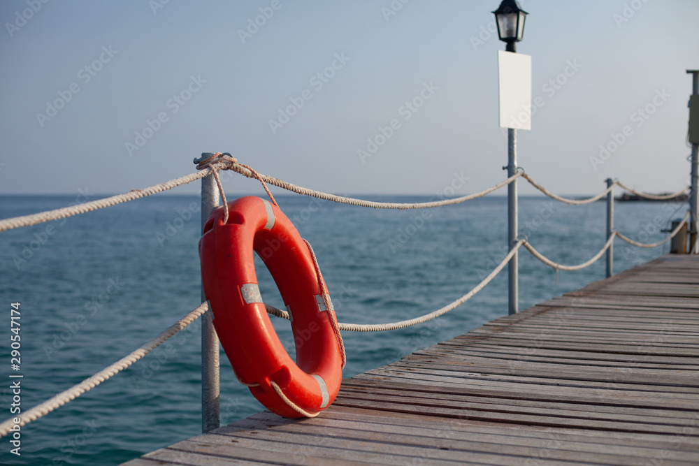 Red life buoy near the fence on a wooden pier. bright sunny weather