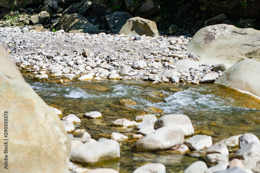 View on a summer sunny day of a waterfall on a stormy mountain river flowing between stones and among the relict forest of the Caucasus Mountains. View on a summer sunny day of a waterfall on a stormy mountain river flowing between stones and among the relict forest of the Caucasus Mountains.