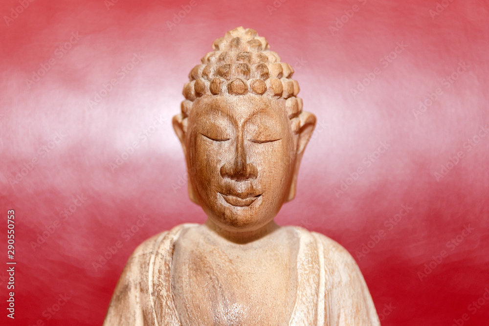 Wooden statue of Buddha, symbol of Buddhism on red background. Free copyspace for text