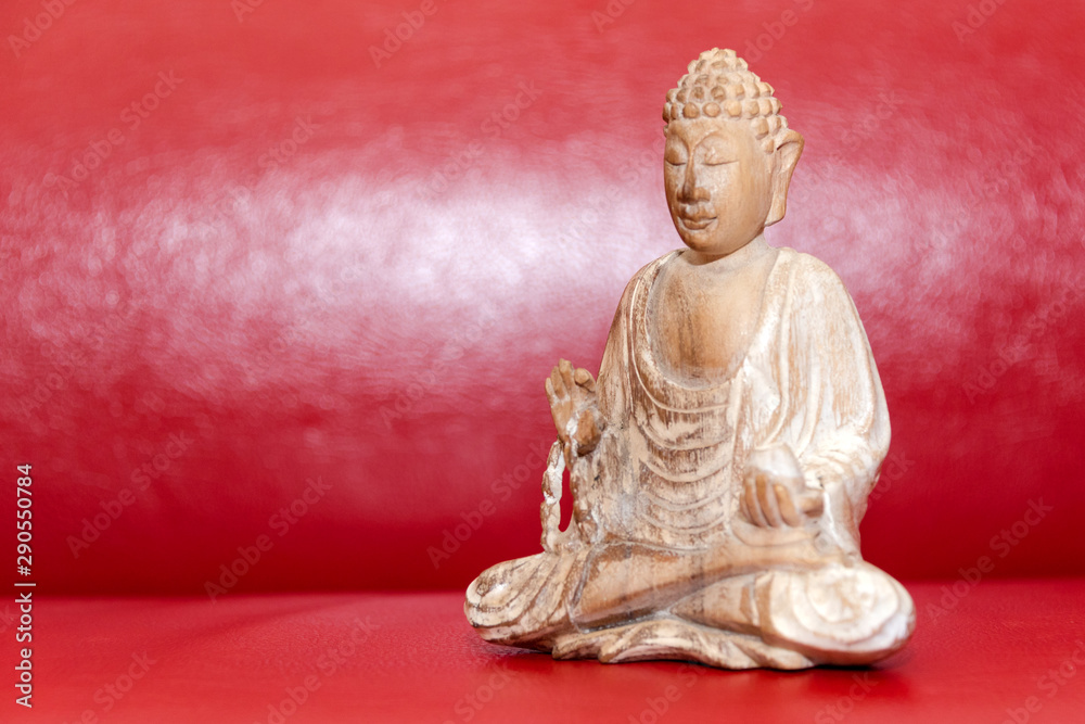 Wooden statue of Buddha, symbol of Buddhism on red background. Free copyspace for text