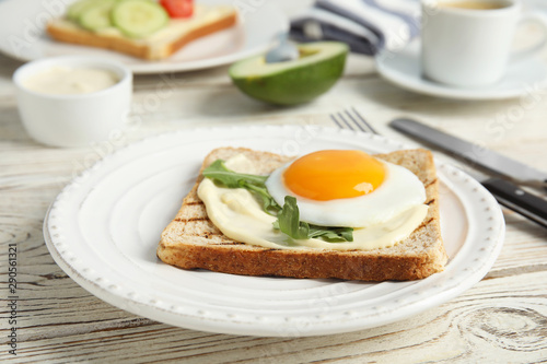 Slice of bread with fried egg, spread and arugula on white wooden table