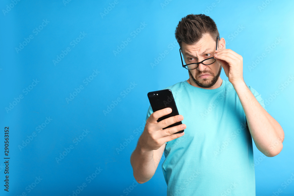 Man with vision problems using smartphone on blue background, space for text Man with vision problems using smartphone on blue background, space for text