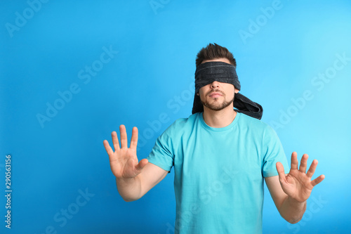 Man with black blindfold on blue background, space for text photo
