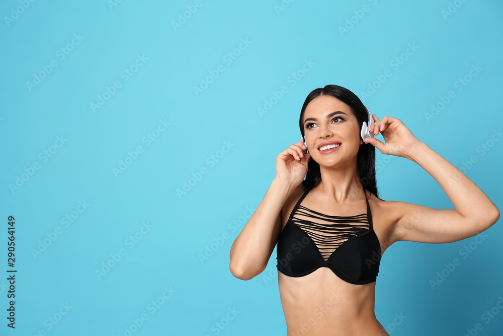Beautiful young woman in black bikini with headphones on light blue background. Space for text Beautiful young woman in black bikini with headphones on light blue background. Space for text