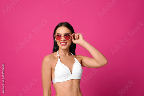 Beautiful young woman in white bikini with sunglasses on pink background