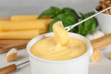 Pot of tasty cheese fondue and products on white wooden table, closeup view