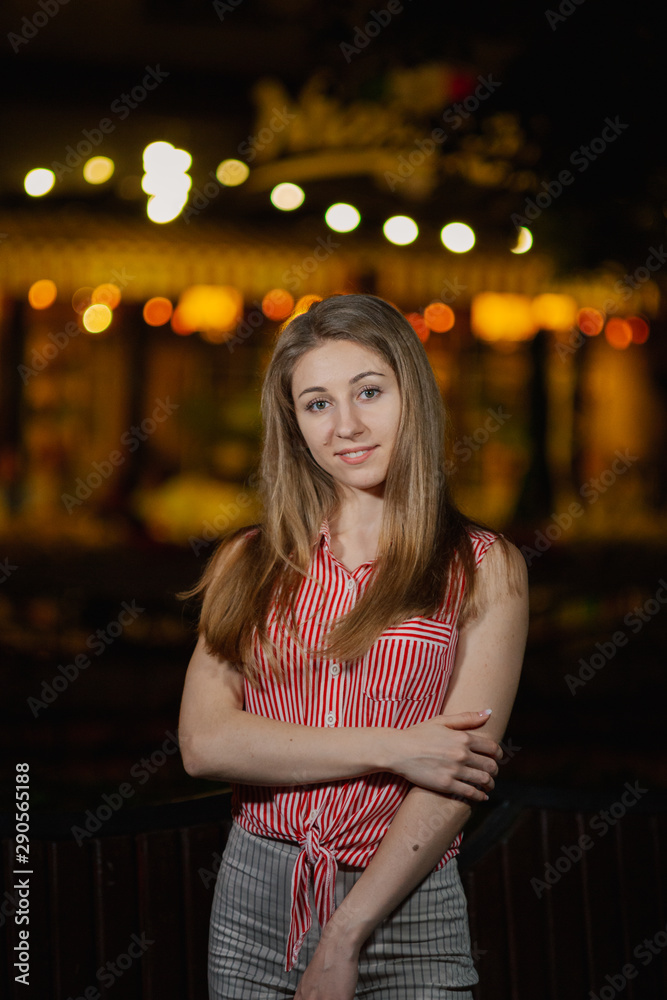 Fototapeta premium Beautiful happy girl in the evening in the park stands with burning lanterns.