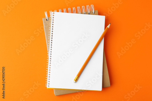 Notebooks with pencil on orange background, top view