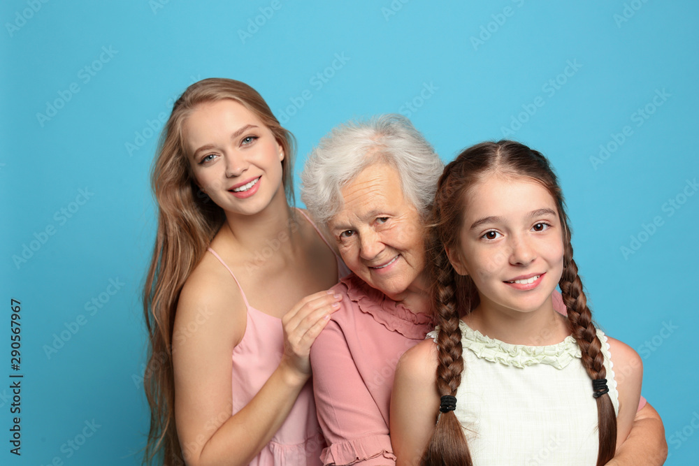 Happy sisters with their grandmother on light blue background