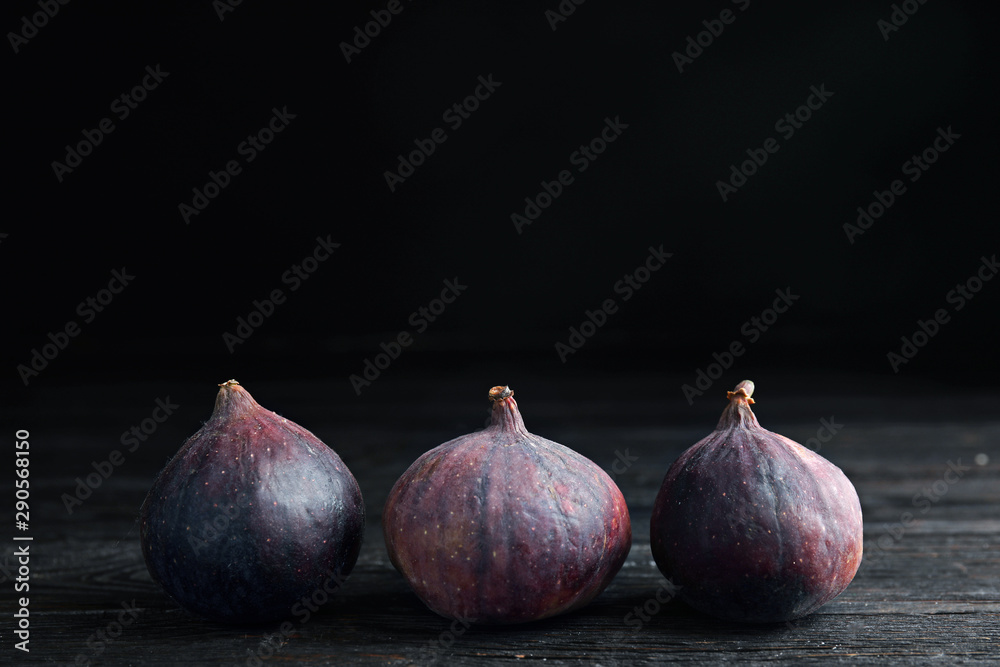 Fototapeta premium Tasty ripe figs on black wooden table against dark background. Space for text