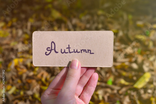 Autumn text on a card. Girl holding card in autumn park in sunny rays.