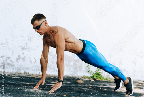 Strong fitness man doing exercise for chest outdoors against concrete wall. Copy space for advertising. Sportsman doing pushups workout outside.