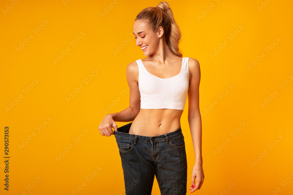 Young Woman In Oversize Jeans Posing, Yellow Background, Studio - obrazy, fototapety, plakaty 