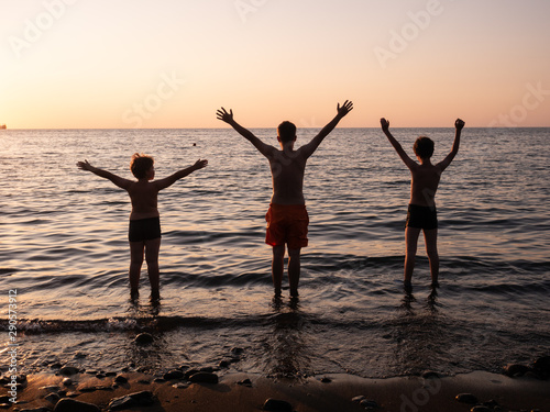 Free happy boys raising arms watching the sun in the background at sea sunrise, teenager on sea