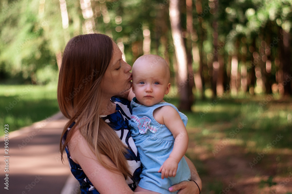 Fototapeta premium Beautiful woman holds one year old baby in her arms in the park. Motherhood and family. Care and development of the child.