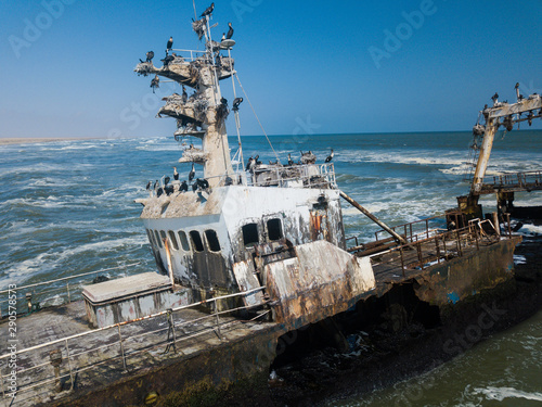 Abandoned and derelict old shipwreck Zeila at the Atlantic Coast near Swakopmund and famous Skeleton Coast in Namibia, Africa. Group of cormorants birds perching on rusted ship. Drone view. photo