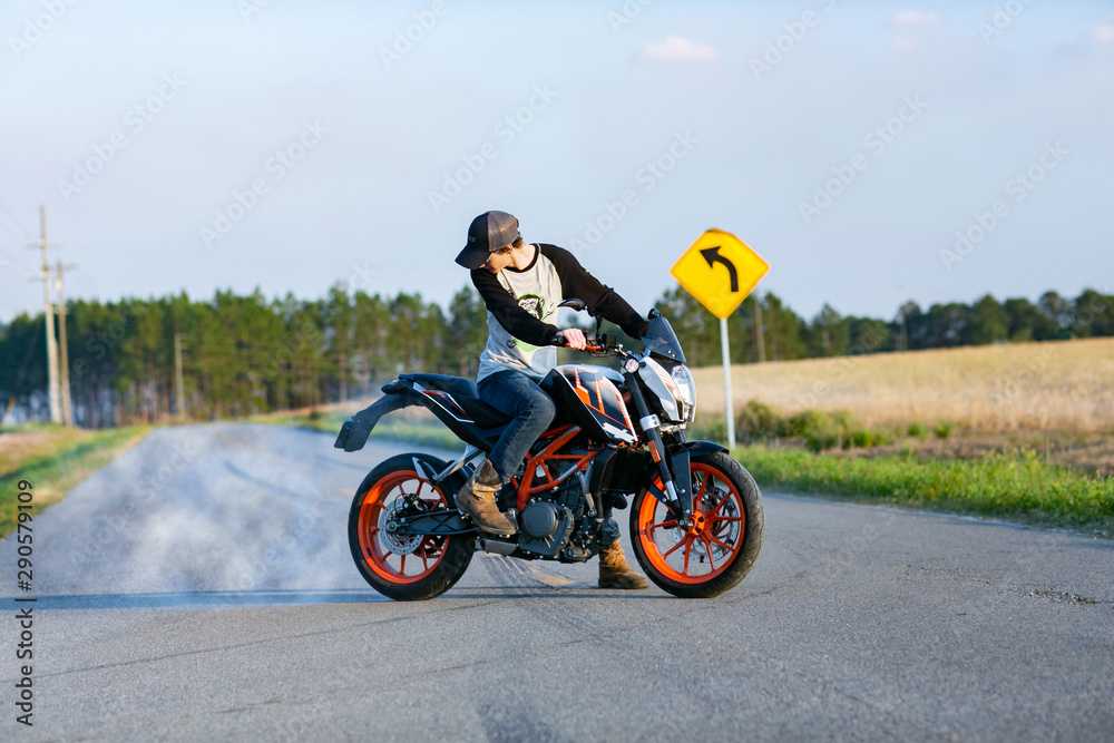 young boy on a country road doing a burnout with a lot of smoke sitting on a motorycle