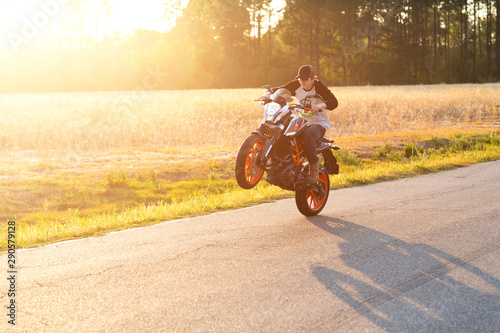 Teenage boy on a dirtbike motorcycle doing a wheelie at sunset photo