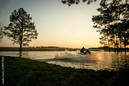 man teen boy riding a personal watercraft and jumping over a peninsula at sunset on a small lake pond
