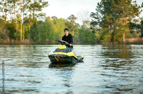 Teenage boy man driving a personal watercraft outside on a lake pond at sunset