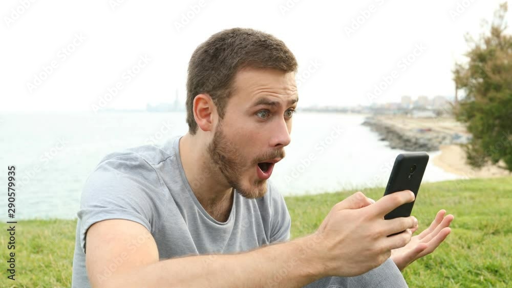 Surprised man checking smart phone messages sitting on the grass Surprised man checking smart phone messages sitting on the grass
