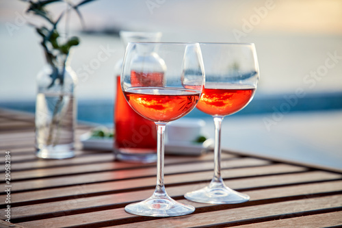 two glasses of rose wine with olives against blue water on a pier..