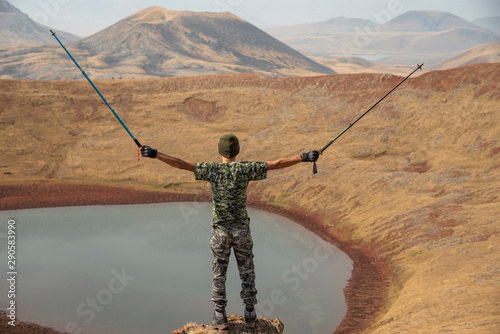 Hiker standing at top of a mountain and looks at the small lake in the crater.