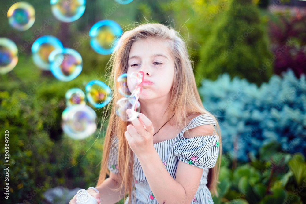 beautiful little girl, teenager, sitting on the bench, blows bubbles. Outdoors