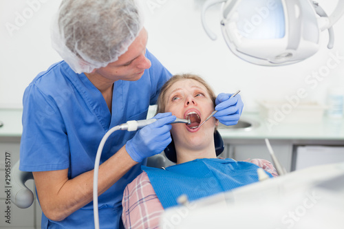Professional dentist examining and performing treatment to young woman