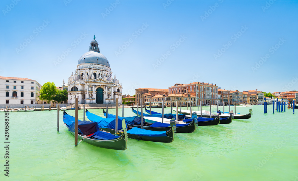 Panoramic view of traditional venetian gondolas moored in water of Grand Canal in front of Basilica di Santa Maria della Salute church, Venice, Italy, in bight sunny day