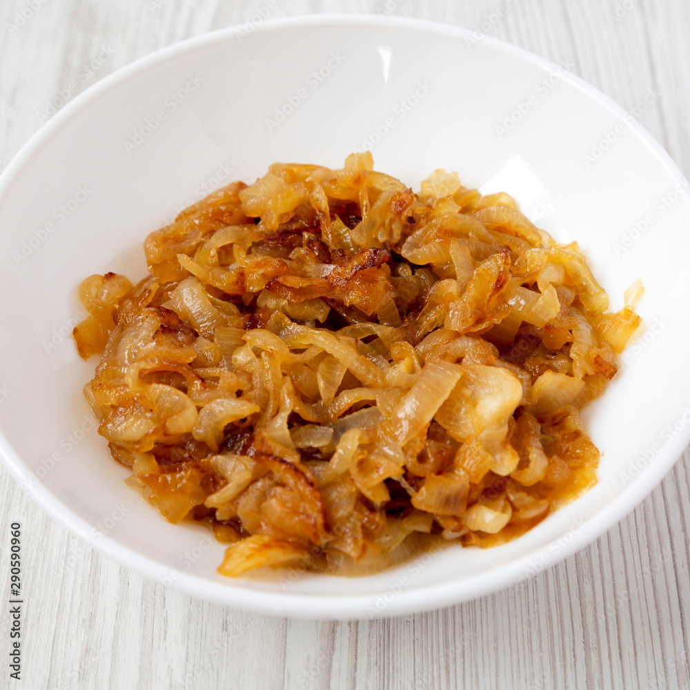 Homemade caramelized onions on a white plate on a white wooden surface, side view. Close-up. Homemade caramelized onions on a white plate on a white wooden surface, side view. Close-up.