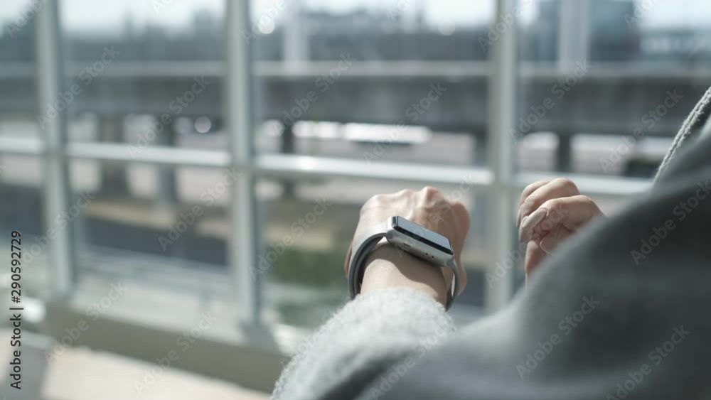 Woman making gestures on a wearable smartwatch computer device, smart watch. Girl in the airport terminal. Woman using smartwatch touchscreen device. Smart watch on female wrist. Surfing internet