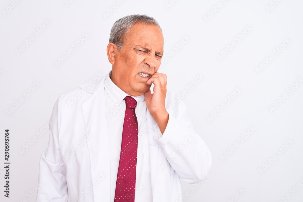 Senior grey-haired scientist man wearing coat standing over isolated white background looking stressed and nervous with hands on mouth biting nails. Anxiety problem. Senior grey-haired scientist man wearing coat standing over isolated white background looking stressed and nervous with hands on mouth biting nails. Anxiety problem.