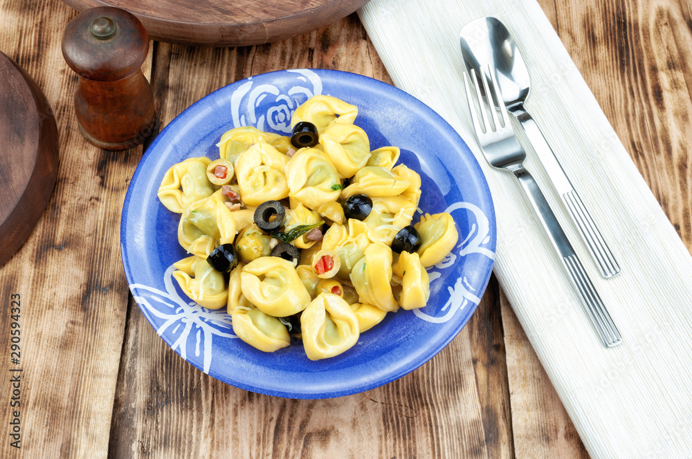 Tortellini with olive on wooden table.