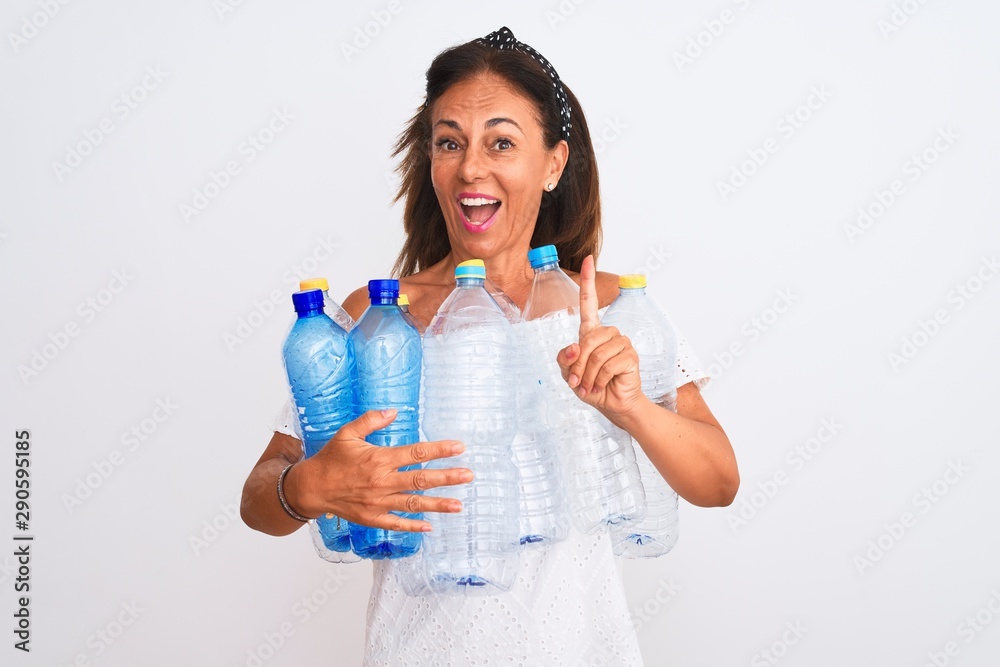 Middle age beautiful woman recycling plastic bottles standing over isolated white background surprised with an idea or question pointing finger with happy face, number one Middle age beautiful woman recycling plastic bottles standing over isolated white background surprised with an idea or question pointing finger with happy face, number one