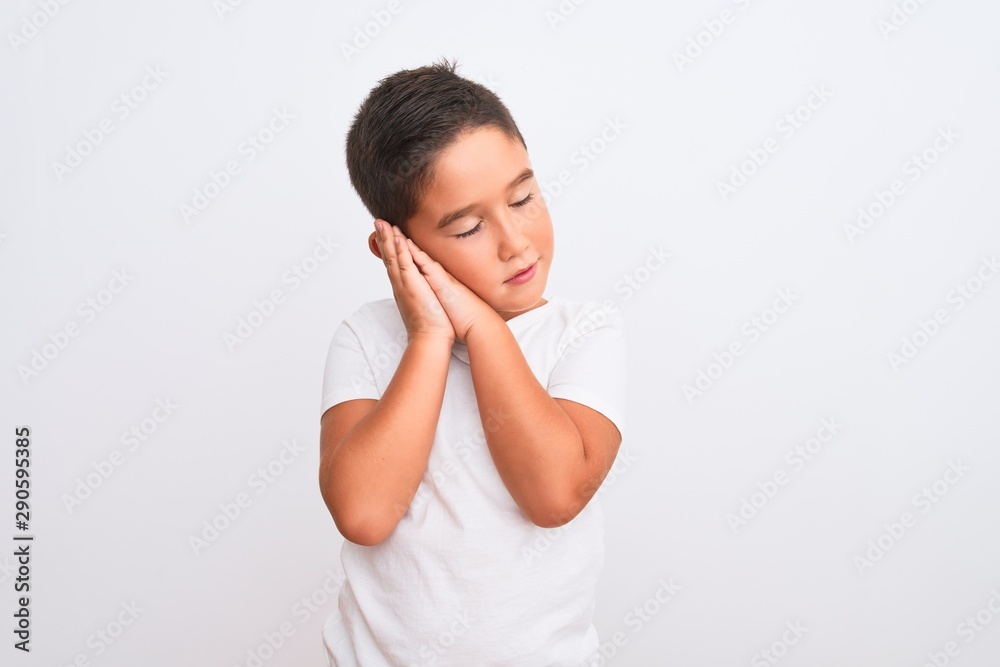 Beautiful kid boy wearing casual t-shirt standing over isolated white background sleeping tired dreaming and posing with hands together while smiling with closed eyes. Beautiful kid boy wearing casual t-shirt standing over isolated white background sleeping tired dreaming and posing with hands together while smiling with closed eyes.
