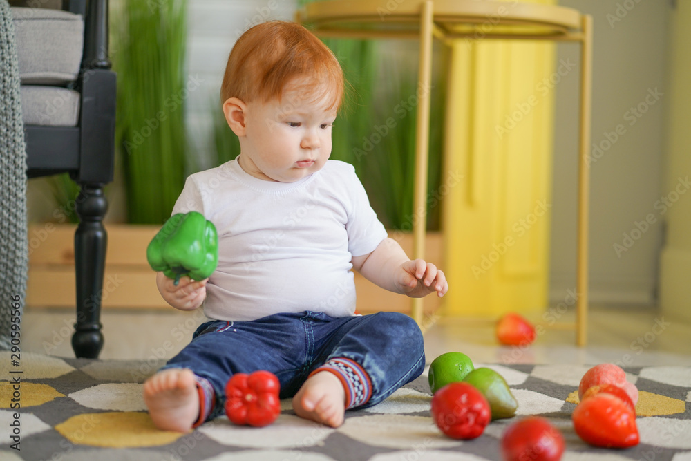 Fototapeta premium chubby fatty baby child with plus size body and red hair plays with vegetables and like his diet on room background