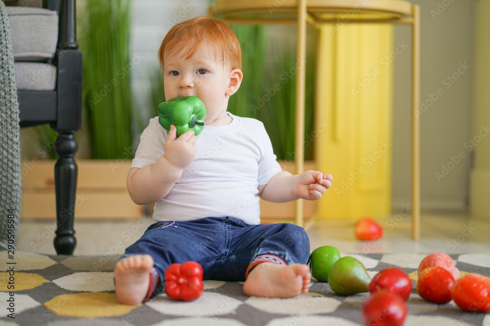 Fototapeta premium chubby child with red hair plays with vegetables