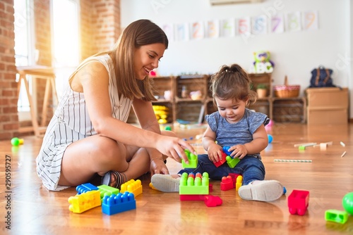 Young beautiful teacher and toddler playing with building blocks toy at kindergarten