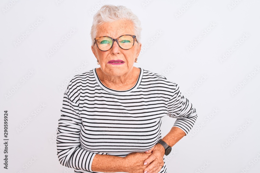 Senior grey-haired woman wearing striped navy t-shirt glasses over isolated white background with hand on stomach because nausea, painful disease feeling unwell. Ache concept. Senior grey-haired woman wearing striped navy t-shirt glasses over isolated white background with hand on stomach because nausea, painful disease feeling unwell. Ache concept.