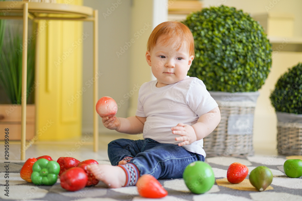 Fototapeta premium chubby child with red hair plays with vegetables