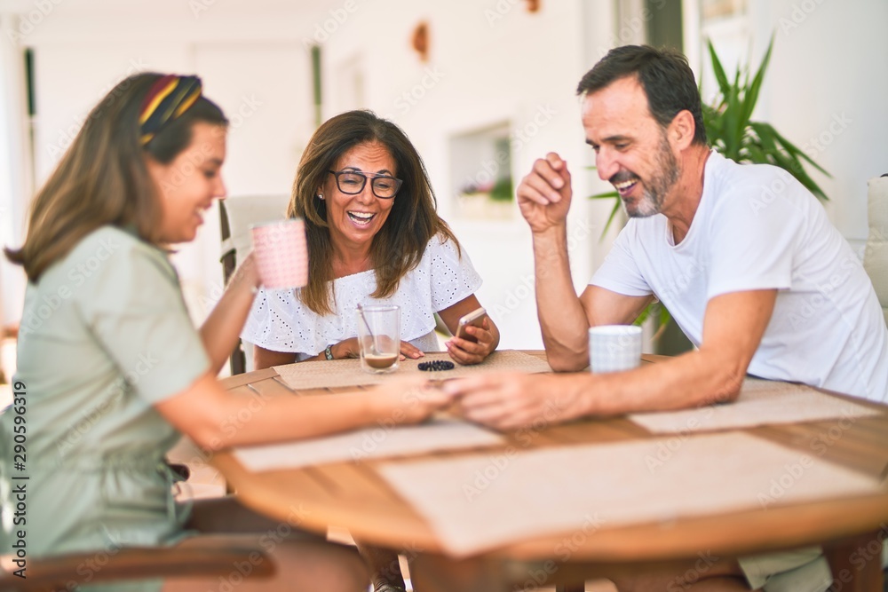 Beautiful family sitting on terrace drinking cup of coffee using smartphone speaking and smiling